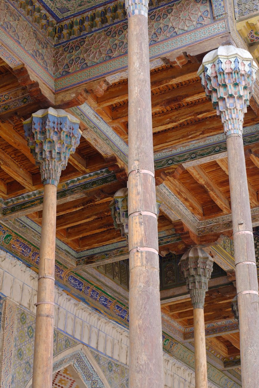 Intricate wooden columns in an ancient mosque with vibrant ceiling details · Bukhara, Uzbekistan