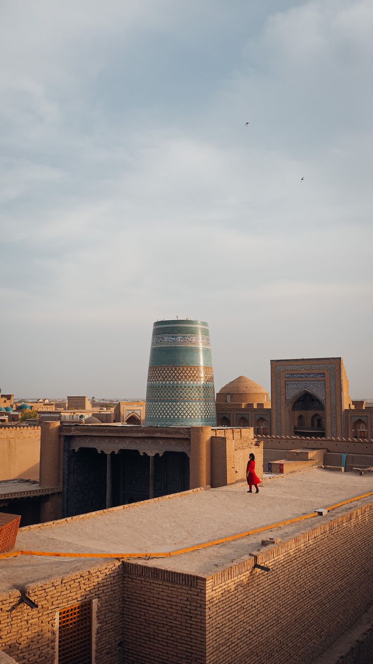 A woman in red walks by the historic Kalta Minor Minaret in Khiva, Uzbekistan
