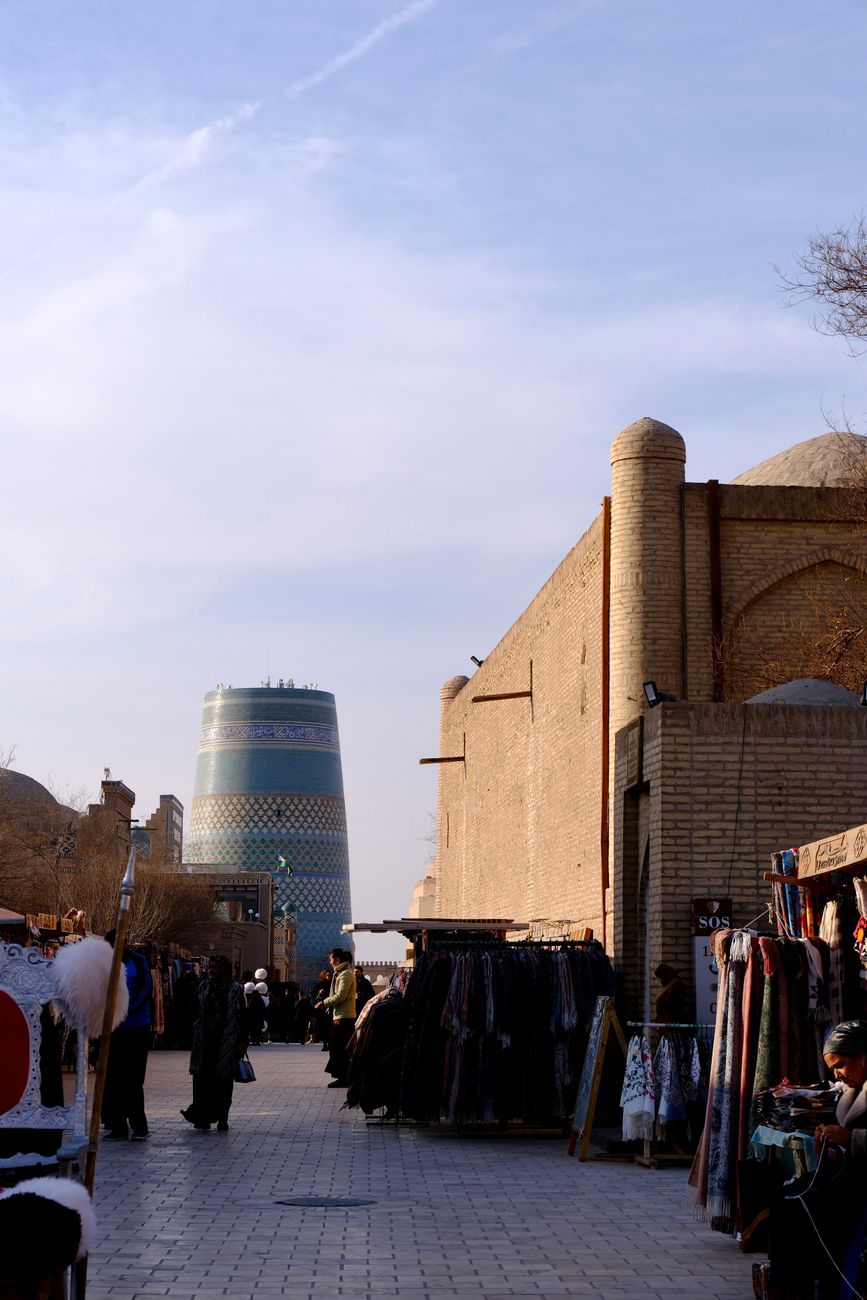 Bustling market street in Khiva with iconic Kalta Minor Minaret visible, capturing local culture, Uzbekistan