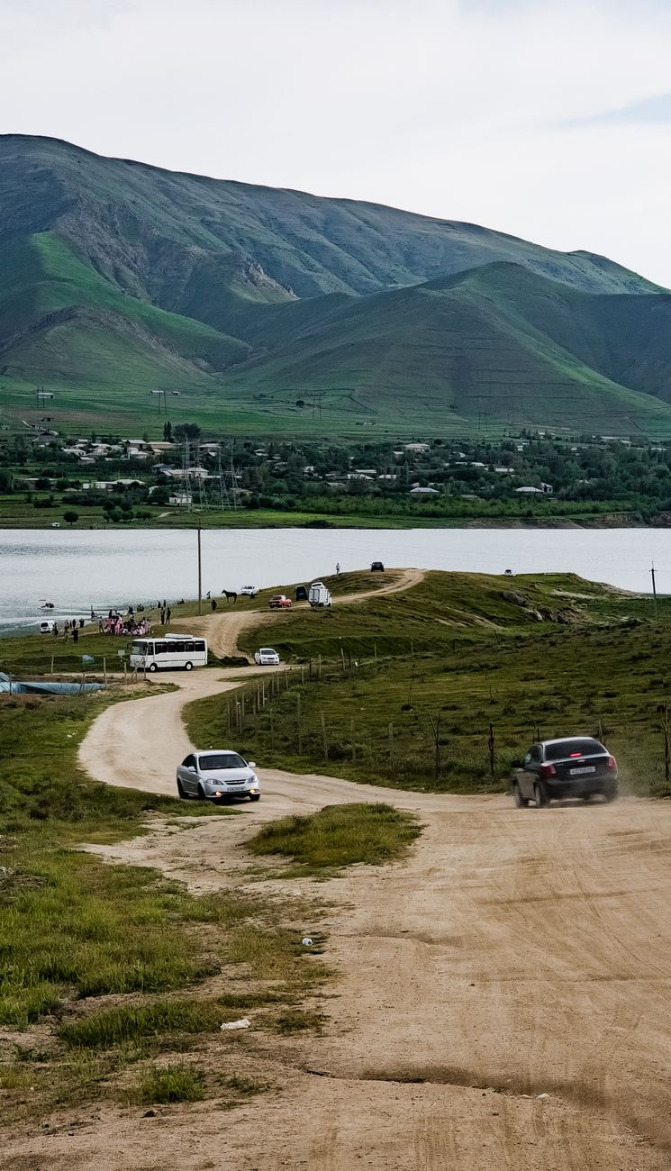Cars on a dirt road by a lake with lush green mountains · Nurata & Aydarkul, Uzbekistan