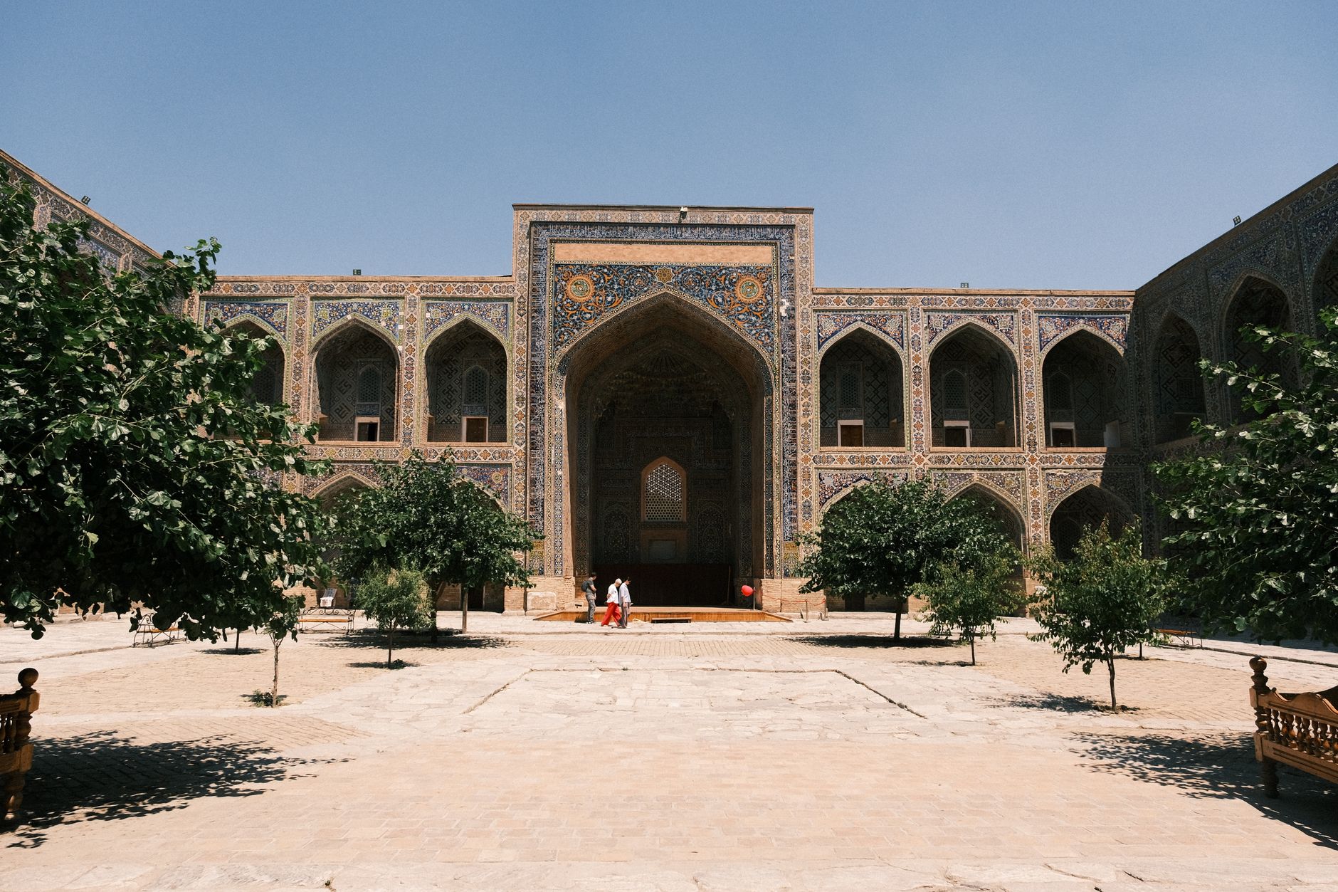 Intricate tilework and grand arches of this historic Islamic courtyard under a clear blue sky, Uzbekistan
