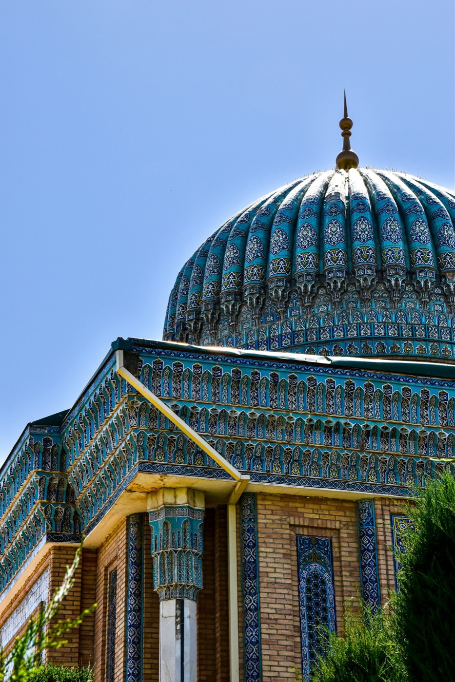 Ribbed turquoise-tiled dome with golden alam finial rising above a densely-tiled mausoleum drum in the Timurid style of Samarkand