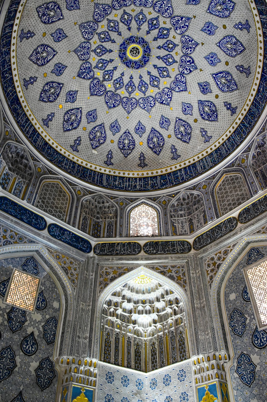 Interior of a Timurid mausoleum dome in Samarkand with dense blue-and-white arabesques, gold accents, and muqarnas transition zones