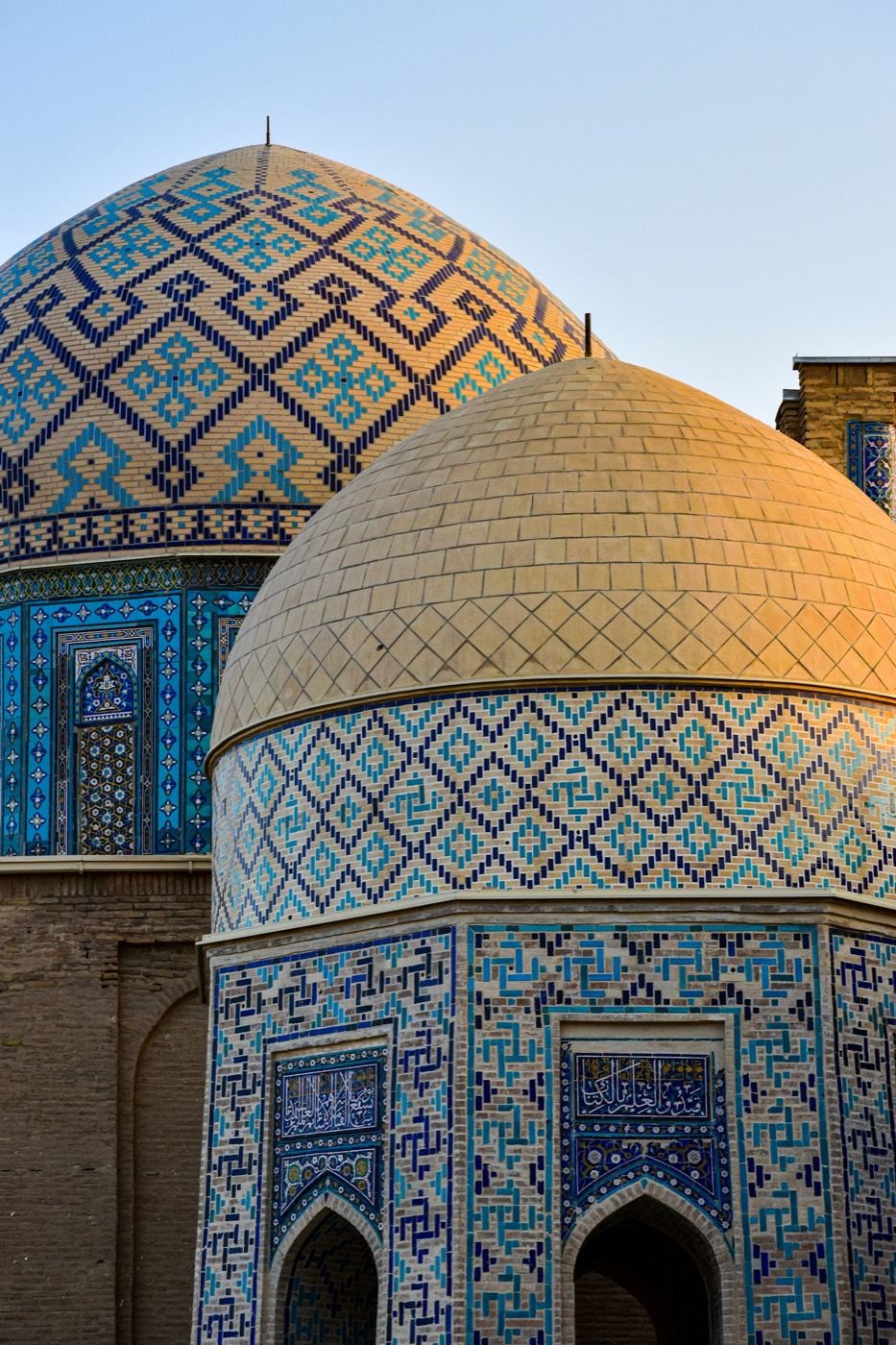 Two brick-and-tile domes over Shah-i-Zinda tombs with geometric diamond patterning and Kufic square-script calligraphy on the drum