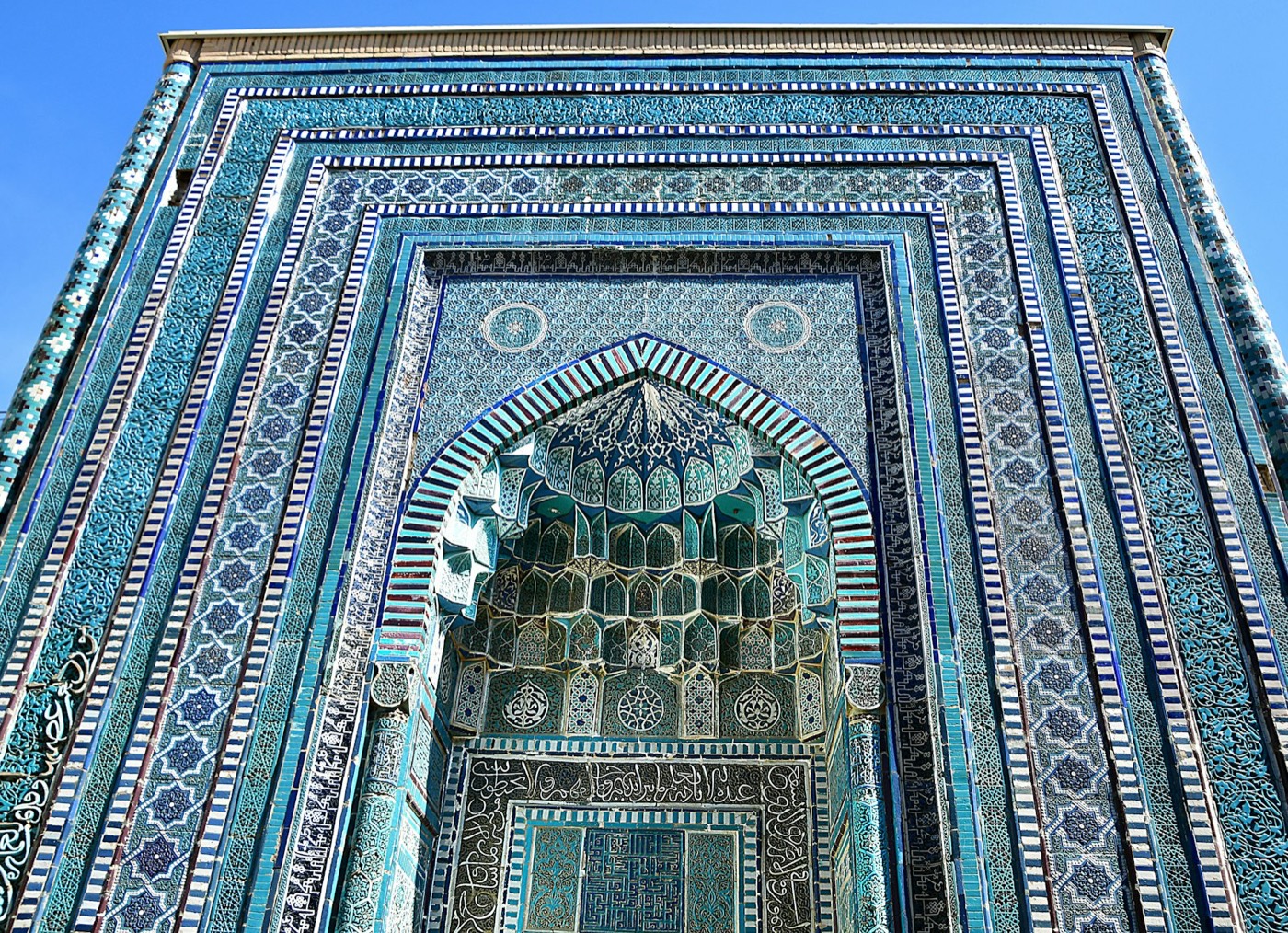 Turquoise-tiled mausoleum portal at the Shah-i-Zinda necropolis in Samarkand, with muqarnas honeycomb vaulting inside a pointed iwan arch